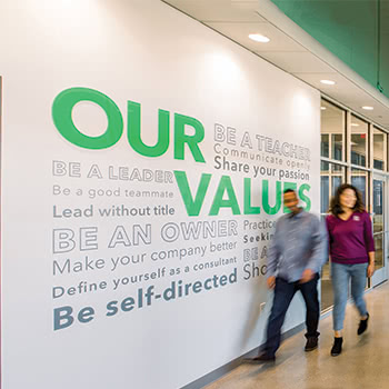 Teammates walking in front of wall that displays Source Allies's values.