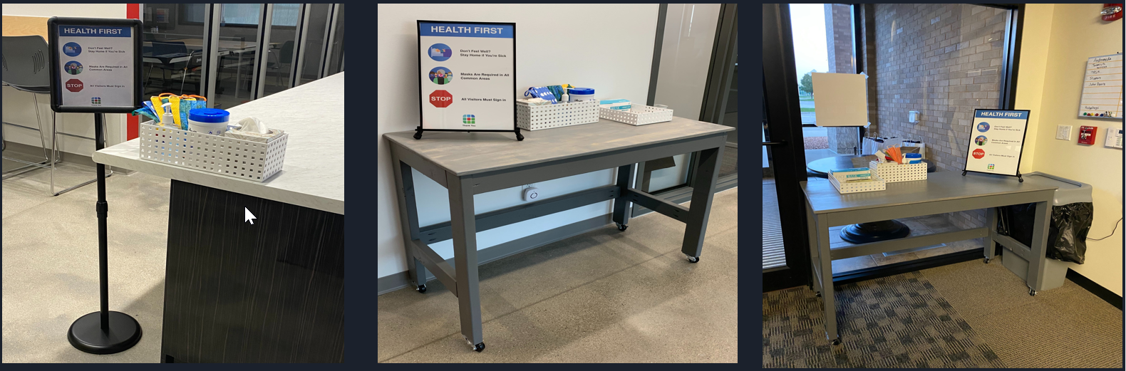 From left to right: single-legged and four-legged stands showing the Source Allies health policy. The 
 four-legged stands also have bins containing masks and wet wipes.
