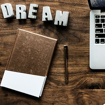 Notepad, pen, laptop, and letters spelling 'DREAM' all sitting on a desk
