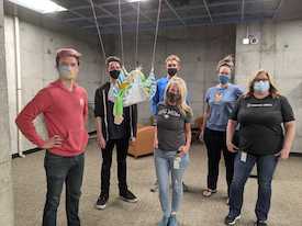 Lounge Lizards team photo posing with their mascot which includes a monkey hanging from the rafters, suspended by a piece of fabric and some yarn.