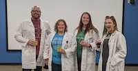 Hackathon organizers dressed in lab coats and holding glass beakers.