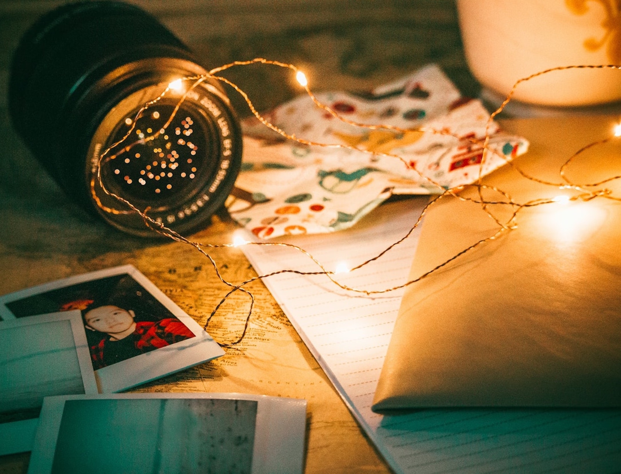 Fairy lights illuminating a work space with photographs and a camera lens.