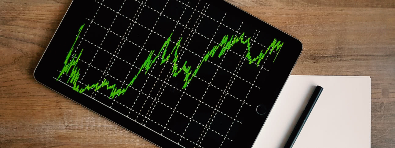 Tablet showing stock prices laying on table with pen and paper