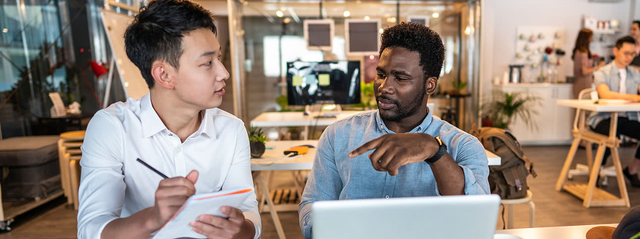 Teammates talking at desk with laptop