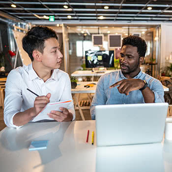 Teammates talking at desk with laptop